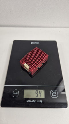 SkyPulse Helios FMU with its heatsink fitted, on a 1 g-resolution scale reading 94 g